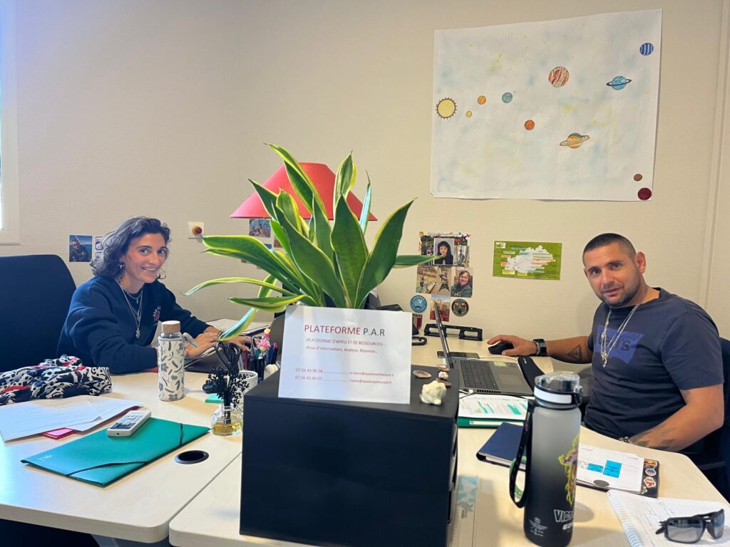 Dans un bureau avec deux personnes fassises derriere leur bureau qui sourient